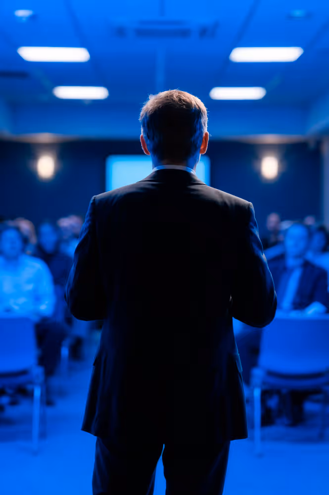 A speaker seen from behind addressing a conference audience